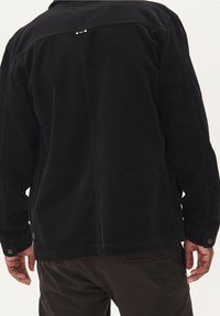 Black corduroy jacket with visible ribbed texture, button cuffs, and a subtle back seam detail. Paired with dark brown pants.