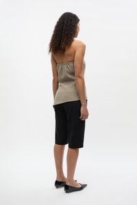 Olivgrübes, trägerloses Oberteil mit gerafftem Ausschnitt, kombiniert mit schwarzen, knielangen Shorts und schwarzen spitzen Ballerinas. Glatte Stofftextur.