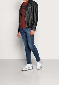 Sort læder bikerjakke, maroon Levi's t-shirt, blå slim-fit jeans og hvide sneakers med brune såler.
