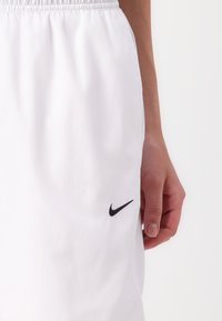 Shorts de sport blancs avec une taille élastique, arborant un logo Nike noir sur le côté gauche. Texture lisse et matériau léger.