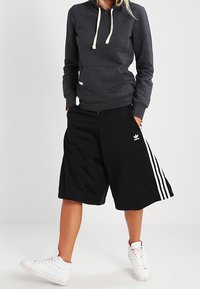 Sweat à capuche gris avec cordons blancs, short de sport noir avec trois bandes blanches, et baskets blanches. Comprend une poche avant et un logo.