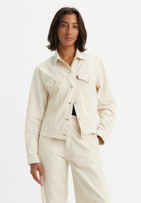 Chaqueta de mezclilla blanca con un diseño ajustado, cuello puntiagudo y cierre de botones. Presenta dos bolsillos en el pecho y detalles de costura sutiles.
