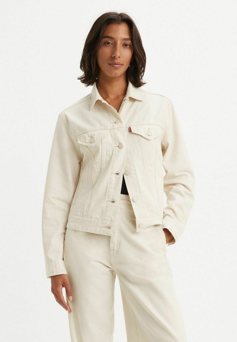 Chaqueta de mezclilla blanca con un diseño ajustado, cuello puntiagudo y cierre de botones. Presenta dos bolsillos en el pecho y detalles de costura sutiles.