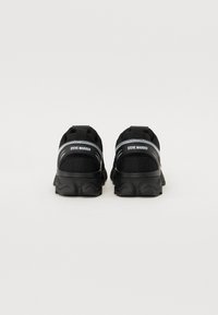 Black athletic shoes with mesh upper, cushioned sole, and reinforced heel. Features branding on the back and curved design accents.