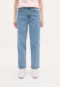 Jean denim bleu clair avec une coupe droite, cinq poches et un détail de broderie subtile. Assorti à des baskets blanches avec des accents roses.