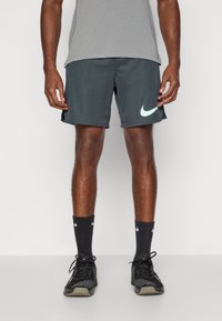 Vīriešu tumši pelēki sporta šorti ar gaiši mentolzaļu Nike logotipu. Izmantojot melnas zeķes un melnus sporta apavus, kuriem ir struktūrēts dizains un elpojošs audums.