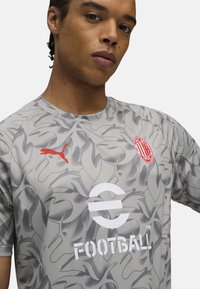 Grå kortærmet fodboldtrøje med camouflage-mønster, rød Puma-logo og hvid tekst "FOOTBALL!" med et cirkulært design.