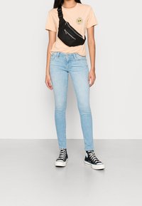 Svart axelväska över en ljusrosa t-shirt med blomgrafik, matchat med ljusblå skinny jeans och svarta högskor.