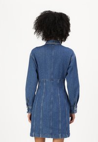 Denim skjortekjole med en figursydd midje, lange ermer og knappede mansjetter. Har bakstykke og vertikal søm. Mørkeblå farge.