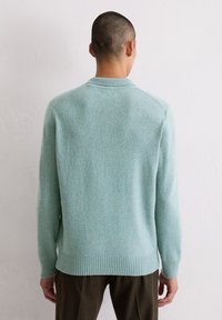 Jasnoniebieski sweter dziany z prążkowanymi mankietami i ściągaczem. Miękka faktura, okrągły dekolt oraz luźny krój, z delikatnym wzorem w cętki.