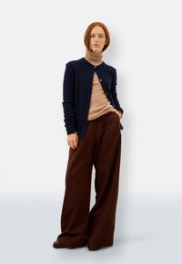 Marinblå cardigan, beige polotröja, bruna vida byxor. Mjuka texturer, knappar på cardiganen, avslappnad passform och rena linjer.