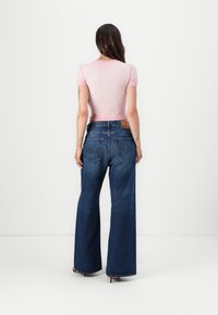 Top justo rosa de manga curta combinado com jeans de perna larga azuis de cintura alta, apresentando um design clássico de cinco bolsos e costura visível.