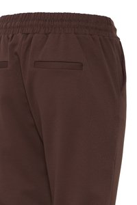 Braune Hose mit elastischem Bund und zwei horizontalen Gesäßtaschen, gezeigt von hinten von der Taille bis zur Mitte des Oberschenkels.