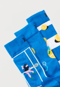 Μπλε κάλτσες με γραφικά τενιστών, μπάλες του τένις και σχέδια γηπέδου. Κατασκευασμένες από απαλό πλεκτό υλικό με αντιθετικές λευκές λεπτομέρειες.