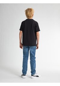 Camiseta negra de manga corta, jeans azules y zapatillas blancas con acentos negros. Ajuste casual con un diseño sencillo y detalles de costura visibles.