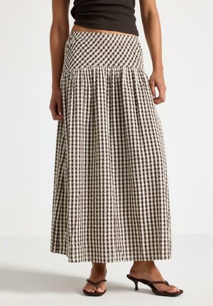 Kvinde iført en sort cropped top, sort og hvid vichyternet lang nederdel og sorte hæle på en ensfarvet baggrund.