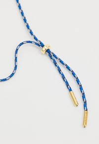 Blaue und weiße geflochtene Schnur mit einem goldenen Schieber und Metallspitzen, die eine strukturierte Oberflächenbeschaffenheit und ein fest gewebtes Design aufweist.