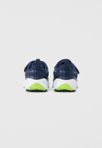 Baskets de sport navy avec un dessus texturé, semelle blanche et accents vert fluo sur le talon et la semelle extérieure. Présente un tirant à l'arrière.