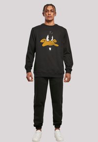 Felpa nera con un grande grafico di Daffy Duck in giallo e bianco. Abbinata a pantaloni jogger neri e sneakers bianche.