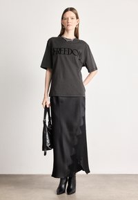 Μαύρη βαμβακερή μπλούζα με το σχέδιο "FREEDOM" εκτυπωμένο σε μαύρο, συνδυασμένη με μια μαύρη σατέν μακριά φούστα με κυματιστό στρίφωμα και λεπτομέρεια δαντέλας. Μαύρες μποτίνες έως τον αστράγαλο και τσάντα.