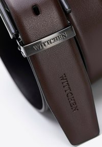 Brązowy pasek z sztucznej skóry z metalowym zapięciem w kolorze srebrnym. Posiada wytłoczone logo "WITTCHEN" oraz teksturowaną powierzchnię. Klasyczny design z eleganckim wykończeniem.