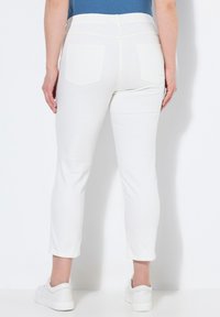 Pantalones blancos hasta el tobillo con una textura suave, que presentan una cintura ajustada, dos bolsillos traseros y un sutil diseño cosido. Combinados con zapatillas blancas.