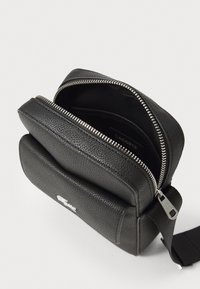Sort læder crossbody taske med en struktureret finish, to rum, sølv lynlås detaljer og en stof skulderrem.