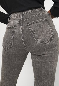 Jeans de mezclilla de tiro alto en gris oscuro con una textura desteñida, dos bolsillos traseros y un ajuste estructurado. Diseño minimalista sin adornos.