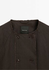 Mörkbrun dubbelknäppt jacka med råa kanter runt kragen och fronten, med fyra knappar och en svart "Massimo Dutti"-etikett inuti.