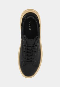 Sneaker in pelle nera con punta arrotondata, lacci frontali e suola in gomma beige. La soletta presenta il nome del marchio "GUESS."