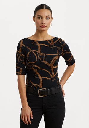 Schwarzes Oberteil mit braunen, reiterlich inspirierten Mustern, kurzen Ärmeln und weitem Ausschnitt. Kombiniert mit hochgeschnittenen schwarzen Jeans und einem Gürtel.