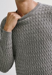 Pull en tricot gris avec un motif torsadé texturé, présentant un col en V et des poignets côtelés, mettant en valeur son tissu doux et sa coupe ajustée.