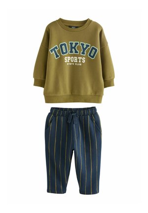 Sudadera verde oliva con el estampado "TOKYO SPORTS STATE CLUB" en azul y blanco. Pantalones de chándal a rayas marino con cintura elástica y bolsillos.