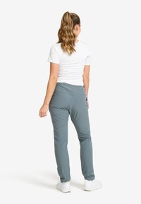 Graue Sporthose mit elastischem Bund und einer seitlichen Tasche, kombiniert mit einem enganliegenden weißen T-Shirt, von hinten betrachtet.