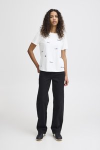 Camiseta blanca de algodón con patrones de texto negro, combinada con pantalones anchos negros y zapatillas negras. Diseño simple y casual con mangas cortas.