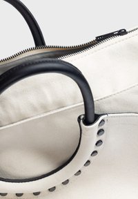 Torba tote z płótna w kolorze off-white z czarnymi skórzanymi uchwytami. Posiada zamek błyskawiczny oraz dekoracyjne czarne ćwieki przy mocowaniu uchwytów.