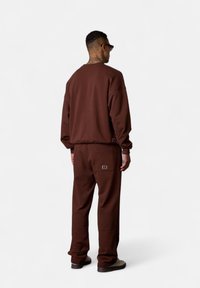 Brown sweat suit made of soft fabric, featuring a crew neck sweatshirt and relaxed-fit pants with side pockets and logo accents.