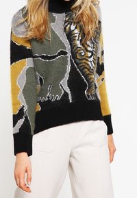 Gestrickter Pullover mit einem Design aus Tiger und Bär in Grün-, Grau-, Schwarz- und Gelbtönen; hoher Kragen und gerippte Bündchen.