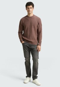 Pull en texture bordeaux avec un col rond, associé à un jean gris foncé et des baskets blanches. Détails notables : motif en tricot et accents subtils.