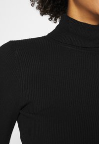 Maglietta nera a collo alto con costine, caratterizzata da un design aderente e un alto colletto, realizzata in tessuto elasticizzato per offrire comfort e calore.