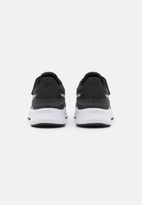 Baskets de sport en mesh noir avec semelles blanches, présentant un dessus texturé, un talon renforcé et une sangle à crochet et boucle pour la fermeture.