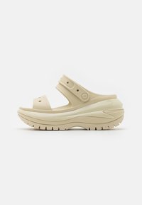 Beige foam sandals with a thick sole, adjustable strap, and textured grip. Open design with prominent ventilation holes.