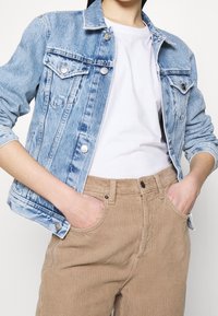 Ljusblå denimjacka med två bröstfickor, metallknappar och blekt textur, tillsammans med tanfärgade kordbyxor med framfickor.