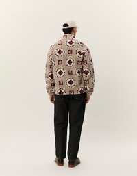 Flis jakna tamne boje s maroon geometrijskim uzorcima. Uparena s tamnim trapericama i smeškim cipelama, prikazana sa leđa.
