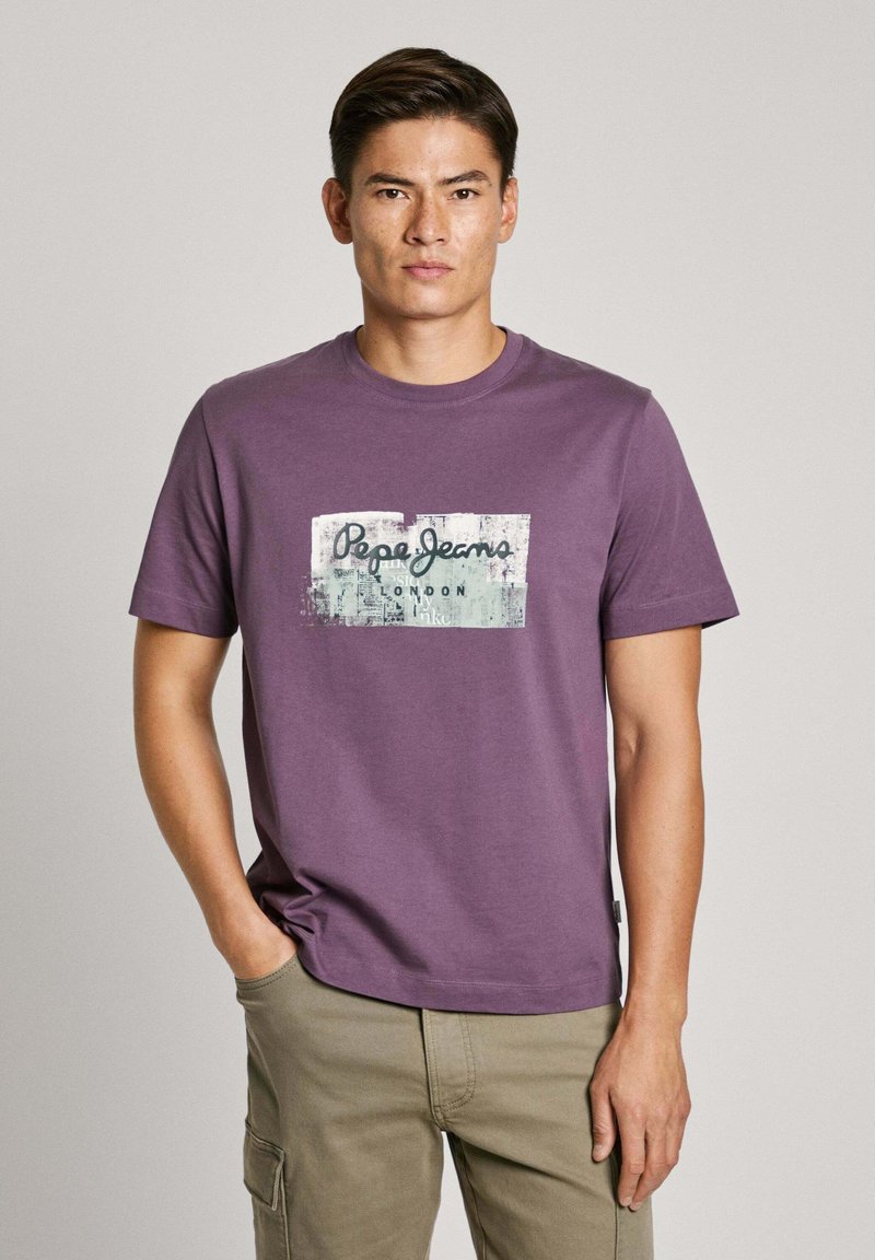 Violetinės spalvos medvilninis marškinėlis su centrinėmis grafikos spaudomis, kuriuose užrašas "Pepe Jeans" ir tekstūruotas fonas. Apvalus kaklas ir trumpomis rankovėmis.