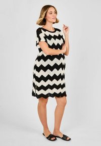 Vestito a zigzag nero e crema con maniche corte, vestibilità rilassata e orlo leggermente svasato. Indossato con sandali neri senza tacco.