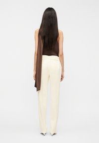 Καφέ αμάνικο τοπ που φοράει πάνω από κρεμ παντελόνι με φαρδύ πόδι. Λείο ύφασμα με ραμμένη εφαρμογή. Διακριτικές λεπτομέρειες στη μέση και στο τελείωμα.