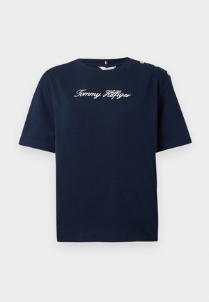 Mørkeblå bomulls T-skjorte med korte ermer, med hvit kursiv "Tommy Hilfiger" logo og gullknappdetaljer på skuldrene.
