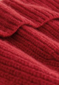 Red, ribbed knit fabric with a fuzzy texture, featuring multiple overlapping layers creating a soft, thick appearance.