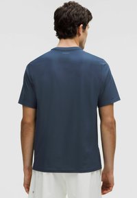 Camiseta atlética azul marino hecha de una tela suave que absorbe la humedad, con cuello redondo y mangas cortas. Presenta un sutil logo en la parte posterior.